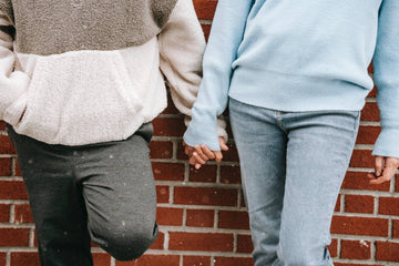 Couple in warm sweaters standing near a brick wall and holding hands