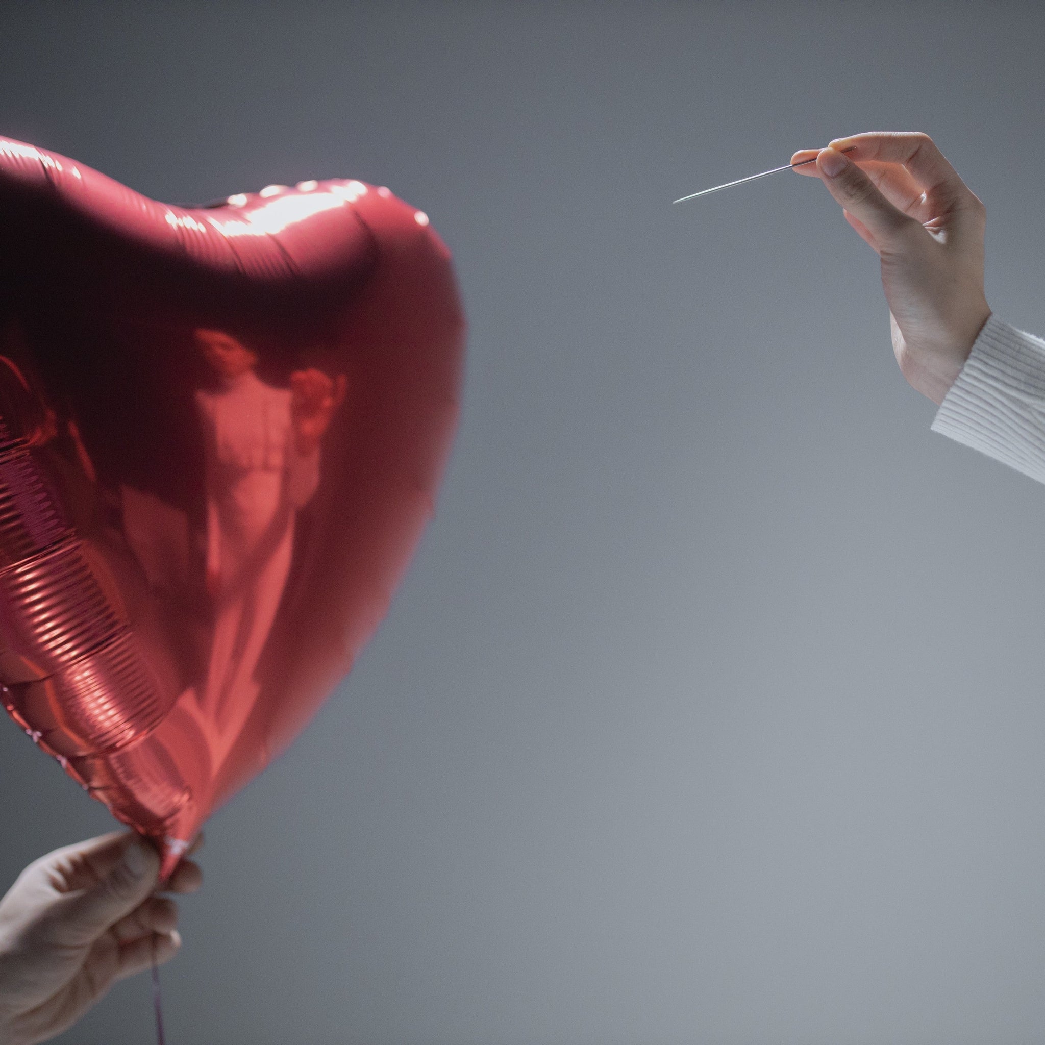 Person Holding Red Heart Balloon And Another Person Holding A Needle