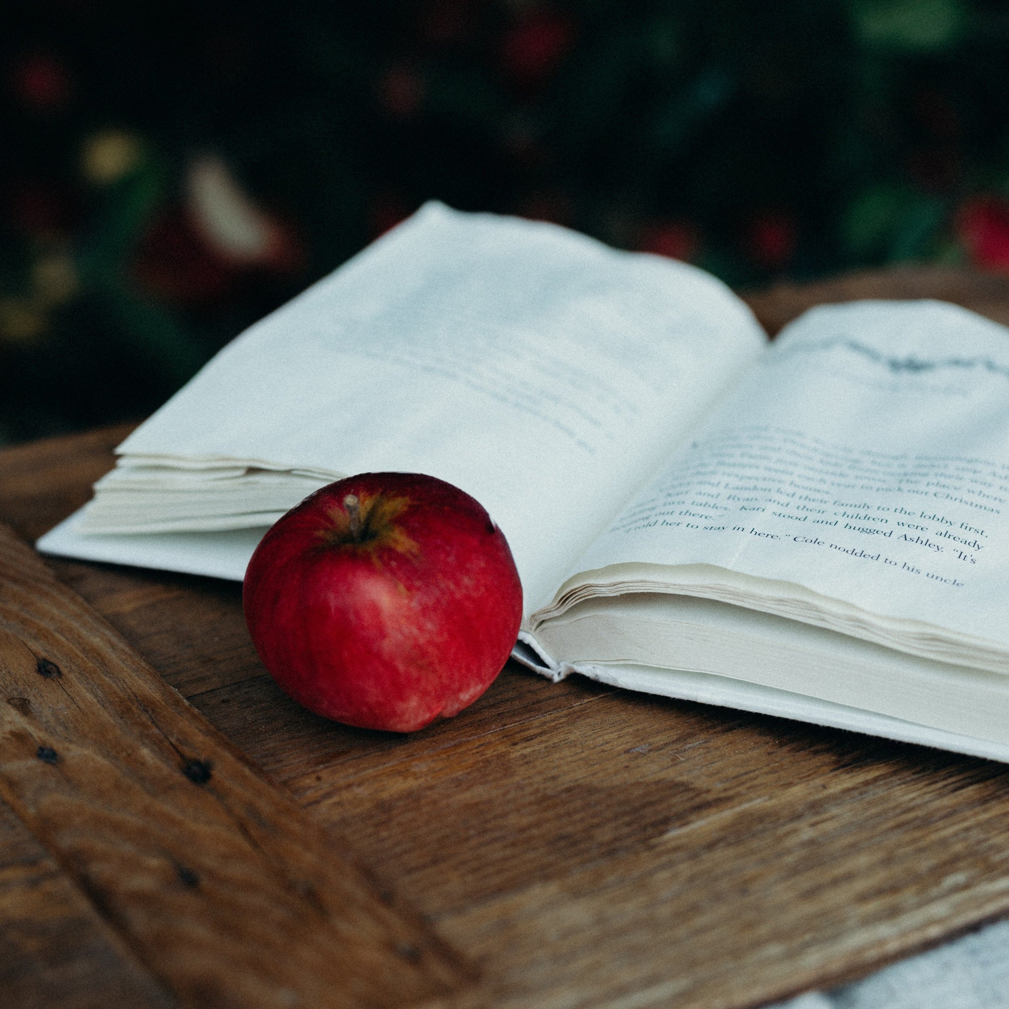 An apple and an open book lying on a wooden table