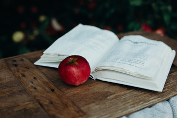 An apple and an open book lying on a wooden table