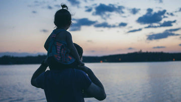 A silhouette of a little girl on her father’s shoulders by the beach