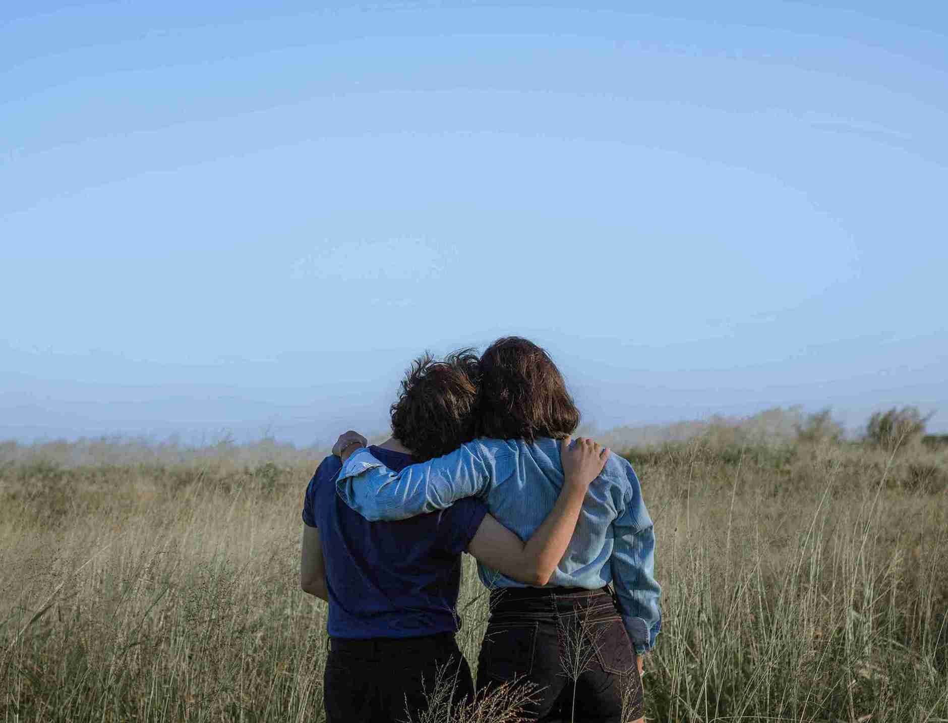 Anonymous female friends embracing on spacious meadow