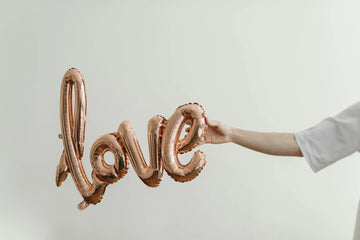 An image of a person holding 'LOVE' balloon to representvalentine's gifts for long-distance boyfriend